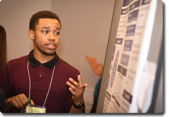 A student involved with the Academic Opportunity Programs, is presenting his research in front of his poster display