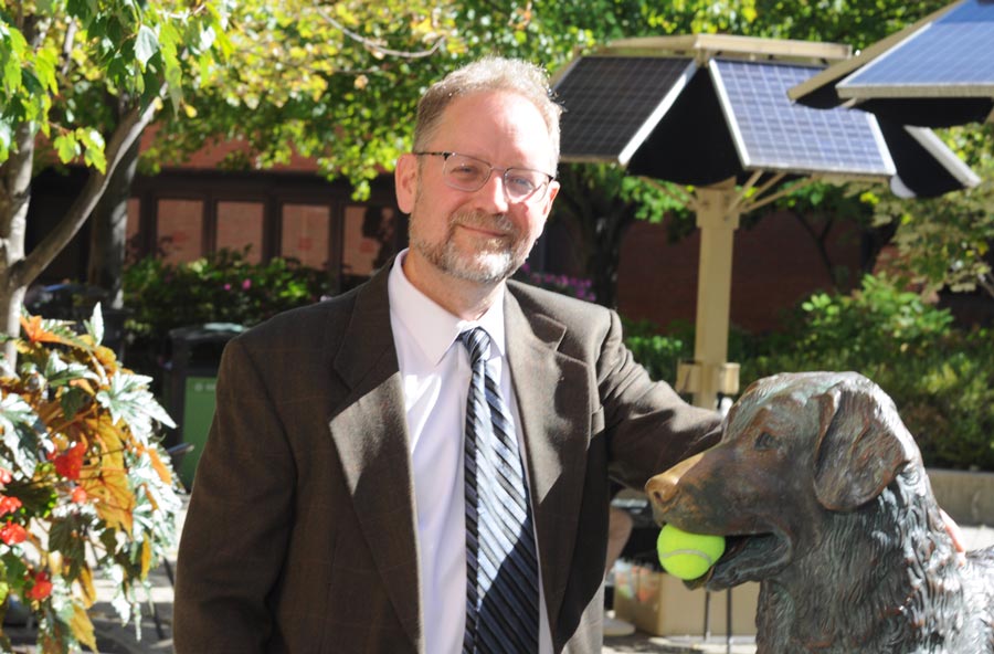 A senior staff member standing next to a staue of the university's mascot