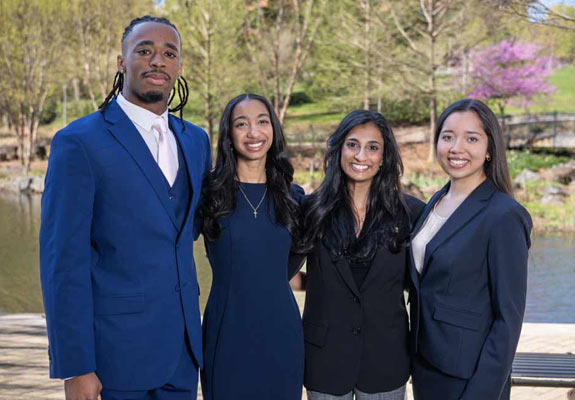 Four students standing in a row dressed in their best, smiling towards the camera